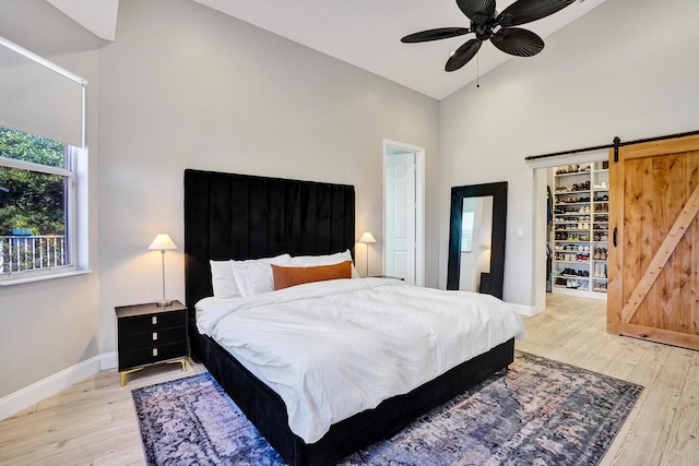 bedroom with high vaulted ceiling, light wood-type flooring, baseboards, a walk in closet, and a barn door