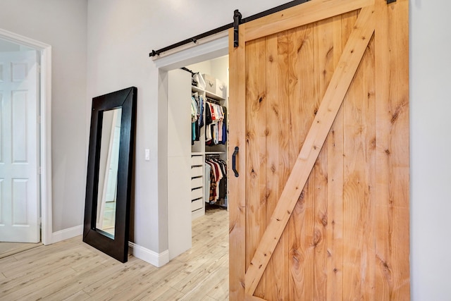 corridor with a barn door, wood finished floors, and baseboards