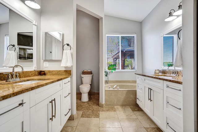 full bathroom with vaulted ceiling, two vanities, toilet, a bath, and baseboards