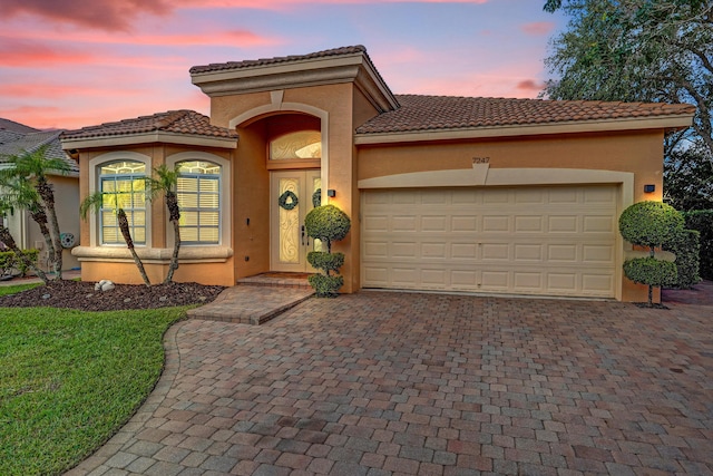 mediterranean / spanish-style house with decorative driveway, stucco siding, a tile roof, and an attached garage