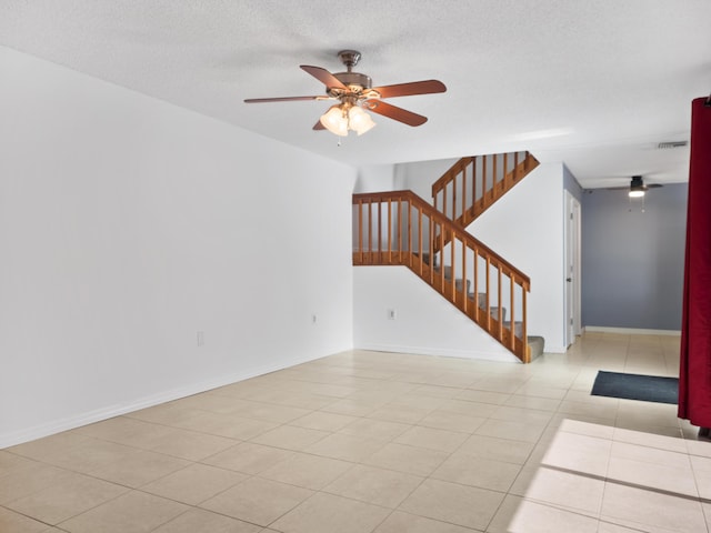 unfurnished living room with ceiling fan, stairway, tile patterned floors, and a textured ceiling