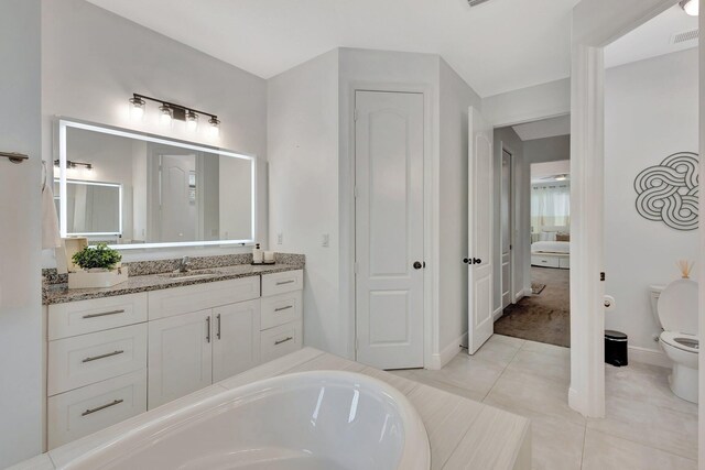 ensuite bathroom featuring toilet, tile patterned flooring, vanity, a tub, and baseboards