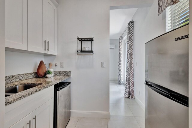 kitchen with light stone countertops, freestanding refrigerator, white cabinets, and light tile patterned floors