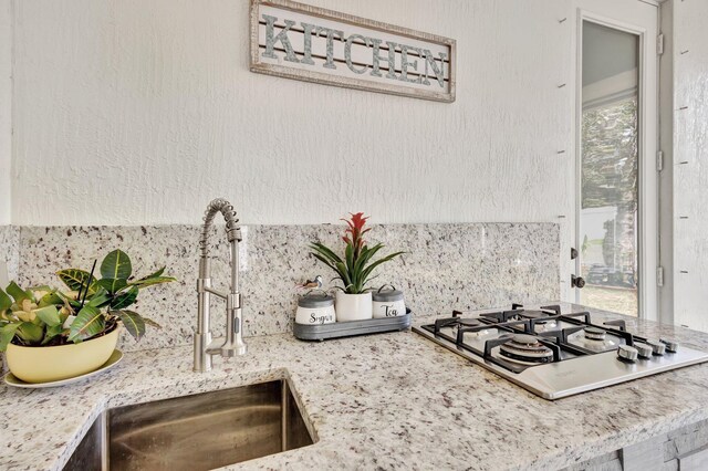 kitchen view of decorative backsplash, a sink, stainless steel gas cooktop, and light stone counters