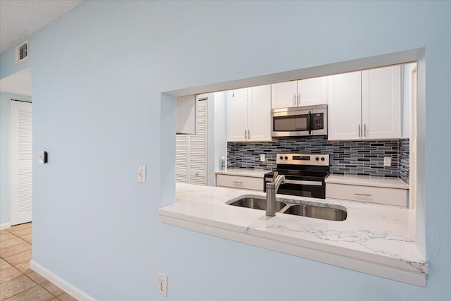 kitchen featuring stainless steel appliances, a sink, tasteful backsplash, light stone counters, and white cabinetry