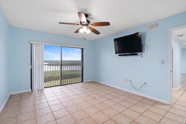 empty room featuring a ceiling fan, baseboards, light tile patterned floors, and a textured ceiling