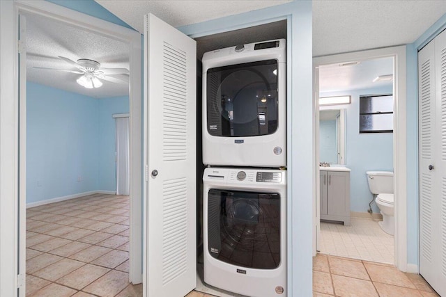 washroom featuring stacked washer / dryer, light tile patterned floors, ceiling fan, a textured ceiling, and baseboards