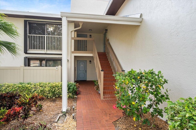 view of exterior entry featuring stucco siding and fence