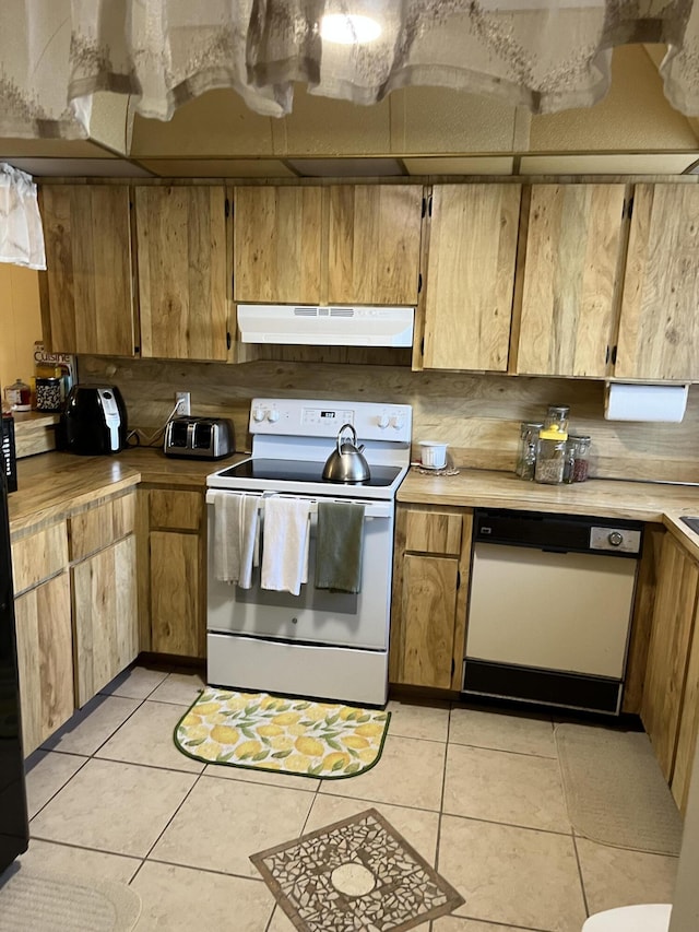 kitchen featuring white appliances, under cabinet range hood, light tile patterned floors, and light countertops