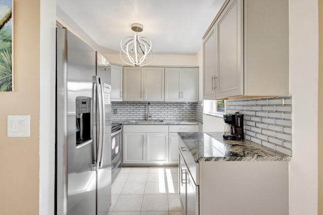 kitchen featuring appliances with stainless steel finishes, a sink, a chandelier, backsplash, and dark stone countertops