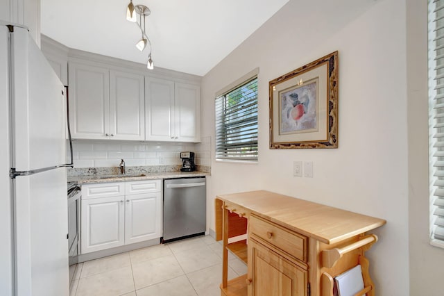 kitchen with appliances with stainless steel finishes, a sink, decorative backsplash, light tile patterned floors, and light stone countertops