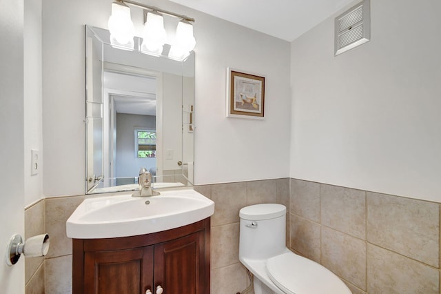 half bathroom with tile walls, toilet, vanity, and a wainscoted wall