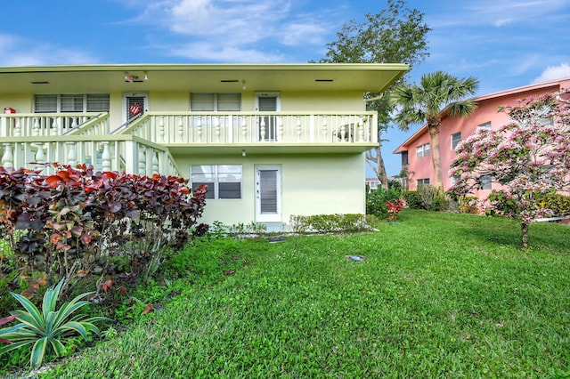 back of property with a balcony, stucco siding, and a yard