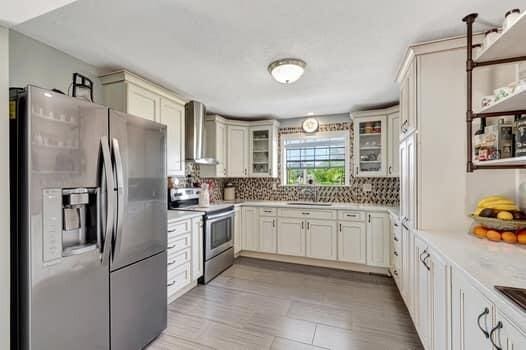 701 SW 1st Ave S, Boynton Beach, FL 33426 - kitchen with stainless steel appliances, wall chimney range hood, backsplash, glass insert cabinets, and a sink
