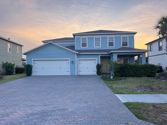 traditional home with decorative driveway, a garage, and a shingled roof