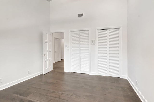 unfurnished bedroom featuring two closets, a high ceiling, baseboards, and dark wood-type flooring