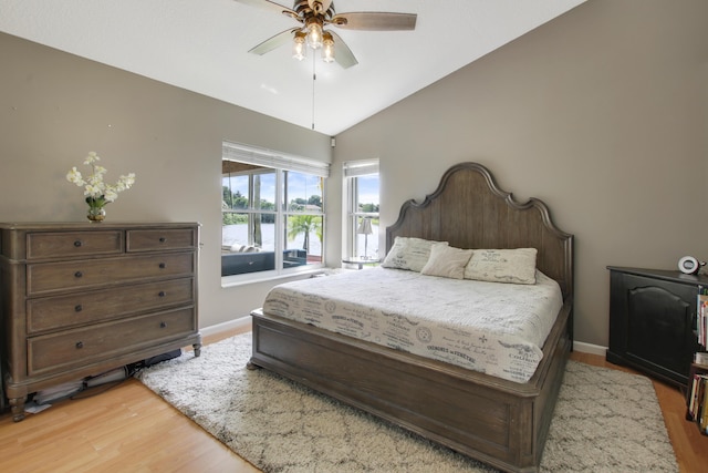 bedroom featuring light wood-style flooring, vaulted ceiling, baseboards, ceiling fan, and a water view