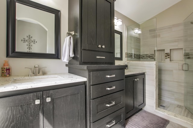 full bathroom with a shower stall, lofted ceiling, and two vanities
