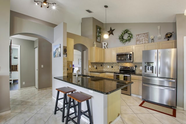 kitchen featuring appliances with stainless steel finishes, a sink, light brown cabinets, arched walkways, and a peninsula
