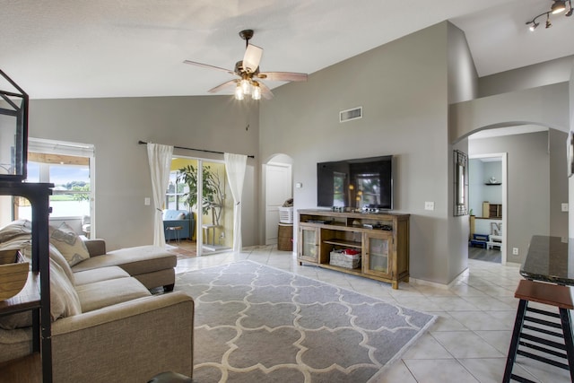 living area featuring arched walkways, light tile patterned flooring, ceiling fan, high vaulted ceiling, and baseboards
