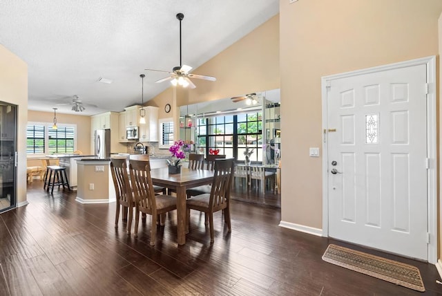 dining room with a ceiling fan, dark wood-type flooring, high vaulted ceiling, and baseboards