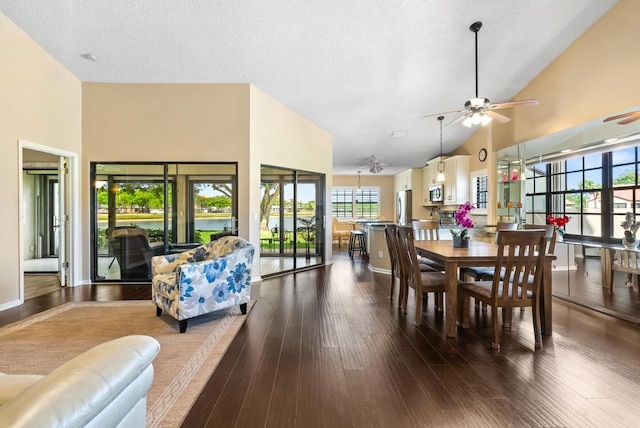 dining area with ceiling fan, high vaulted ceiling, plenty of natural light, dark wood finished floors, and a water view