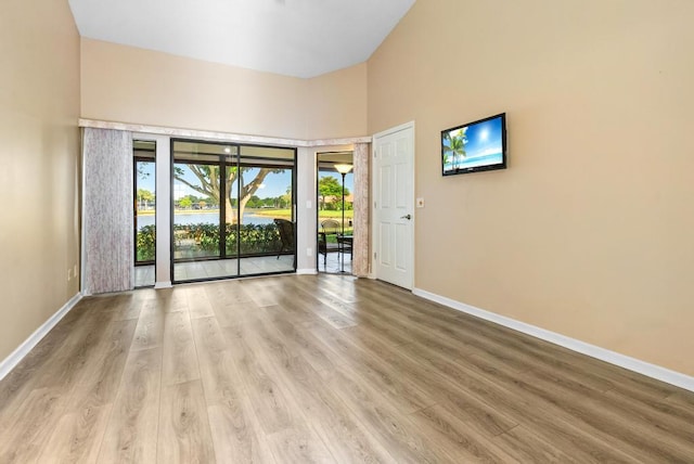 spare room featuring baseboards, wood finished floors, and a high ceiling