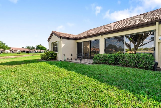 rear view of house featuring a tile roof, a yard, stucco siding, and a patio area