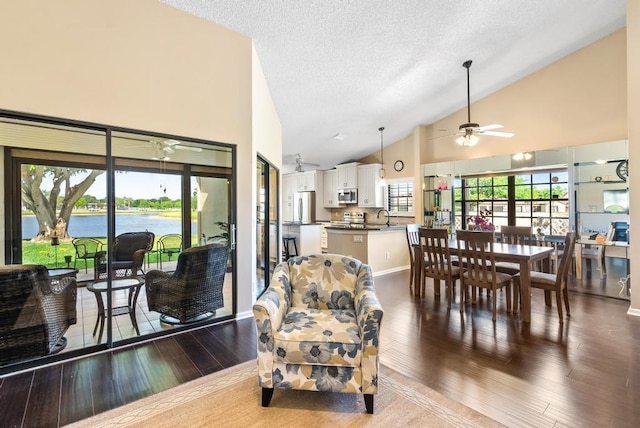 living room with ceiling fan, dark wood-type flooring, high vaulted ceiling, a textured ceiling, and a water view