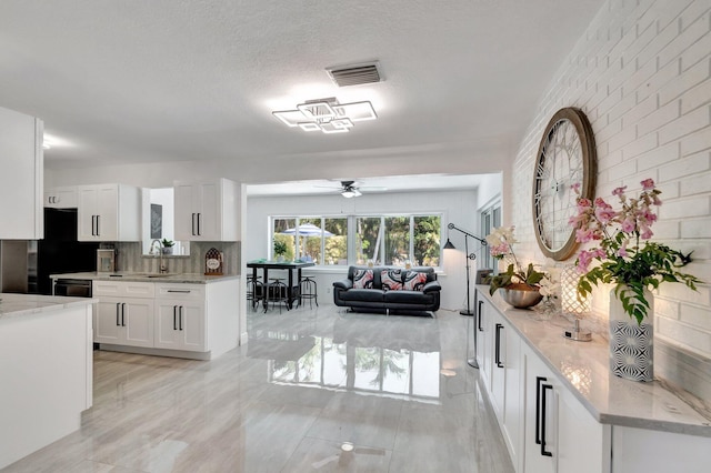 kitchen with a sink, a ceiling fan, white cabinetry, decorative backsplash, and light stone counters