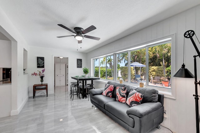 living room with plenty of natural light, ceiling fan, a textured ceiling, and light marble finish flooring