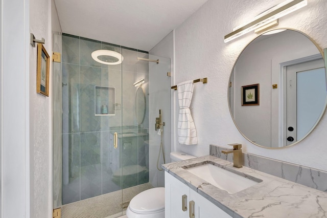 bathroom with toilet, a stall shower, a textured wall, and vanity