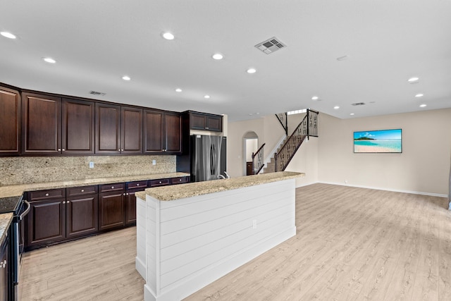 9226 Dupont Pl, Wellington, FL 33414 - kitchen featuring freestanding refrigerator, arched walkways, an island with sink, light wood-type flooring, and decorative backsplash