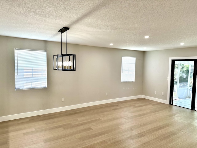 unfurnished dining area with light wood finished floors, recessed lighting, a chandelier, baseboards, and a textured ceiling