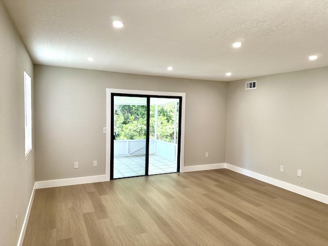 empty room with light wood finished floors, recessed lighting, baseboards, and a textured ceiling