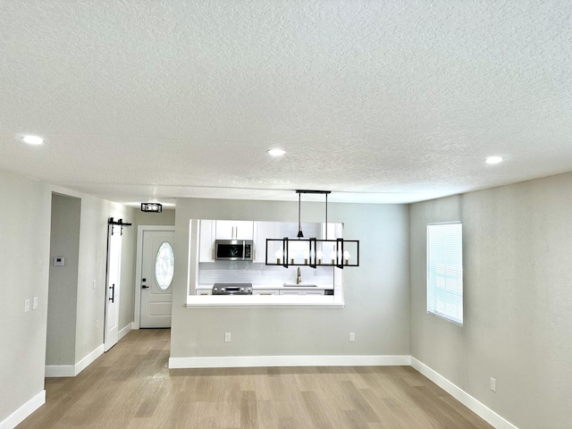 kitchen with stainless steel appliances, light wood-type flooring, a barn door, white cabinets, and a textured ceiling