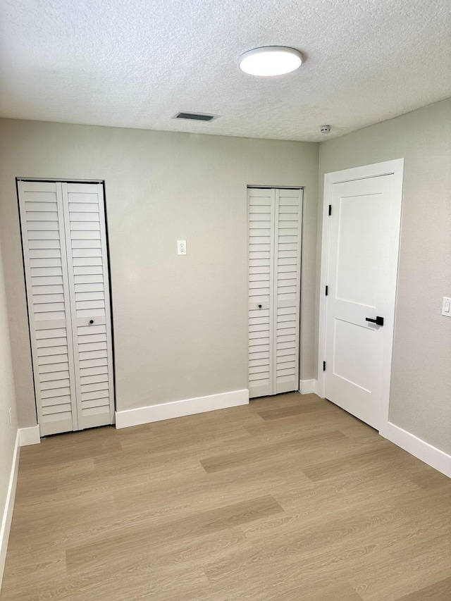 unfurnished bedroom featuring light wood-type flooring, a textured ceiling, and baseboards