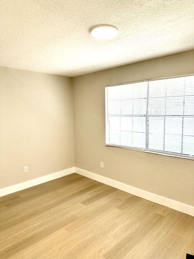 spare room featuring wood finished floors, baseboards, and a textured ceiling