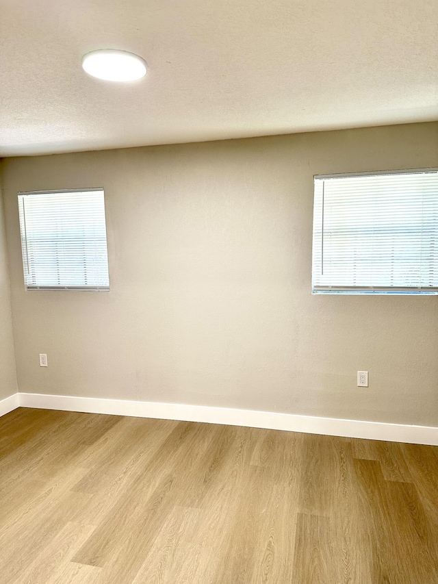 spare room featuring baseboards, wood finished floors, and healthy amount of natural light