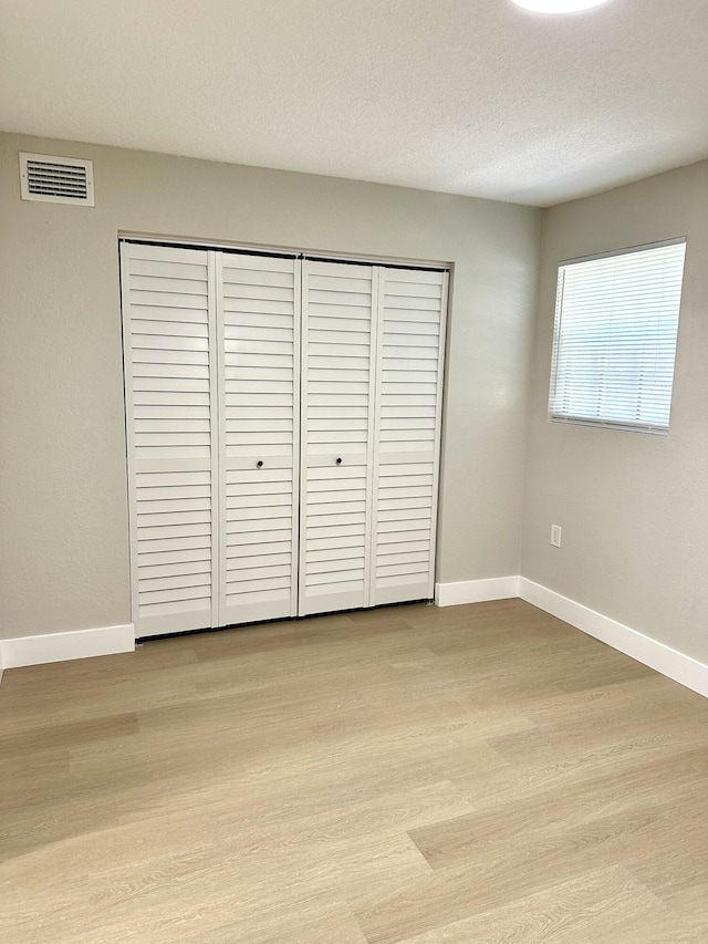 unfurnished bedroom featuring baseboards, a closet, light wood-style floors, and a textured ceiling