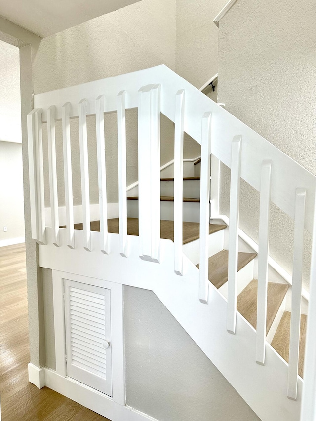 staircase with wood finished floors, a textured wall, and baseboards
