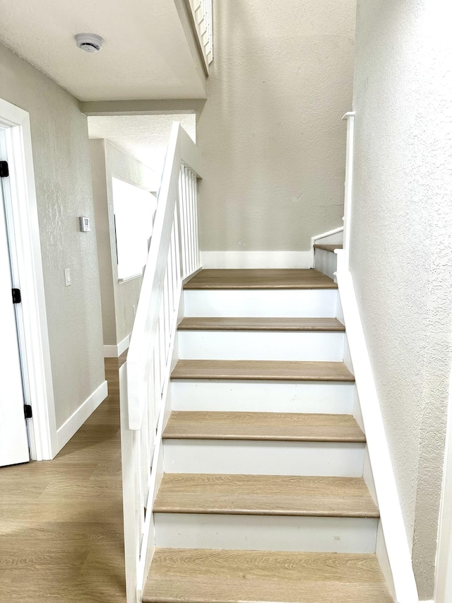 stairs featuring a textured wall, wood finished floors, and baseboards