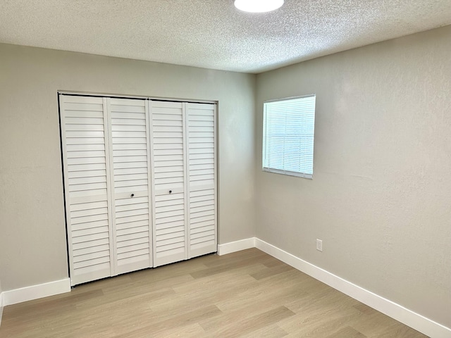 unfurnished bedroom with light wood finished floors, a textured ceiling, a closet, and baseboards