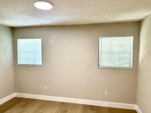spare room with wood finished floors, baseboards, and a textured ceiling