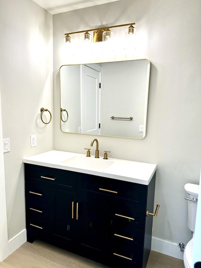 half bath with baseboards, vanity, wood finished floors, and toilet