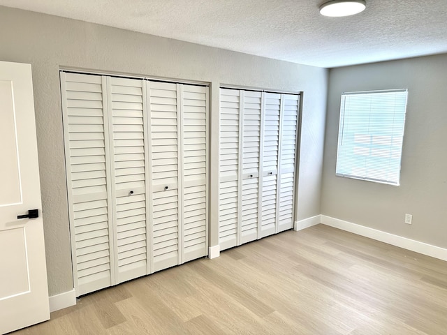 unfurnished bedroom with wood finished floors, a textured ceiling, baseboards, and a textured wall