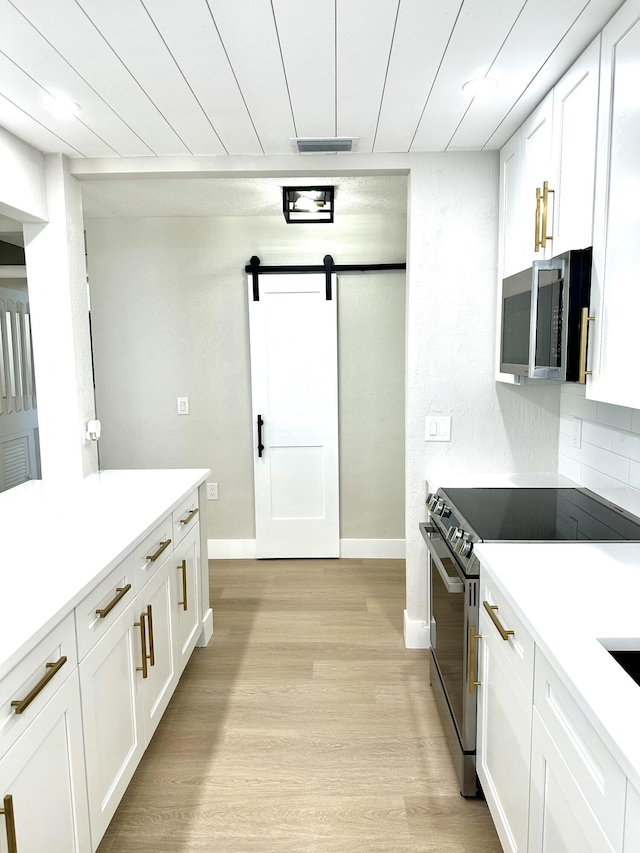 kitchen featuring stainless steel appliances, a barn door, white cabinetry, and light wood-style floors