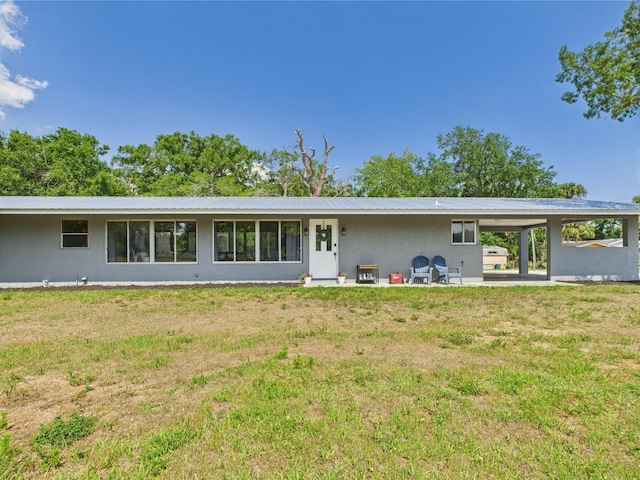 back of property with stucco siding, a lawn, metal roof, and a patio area