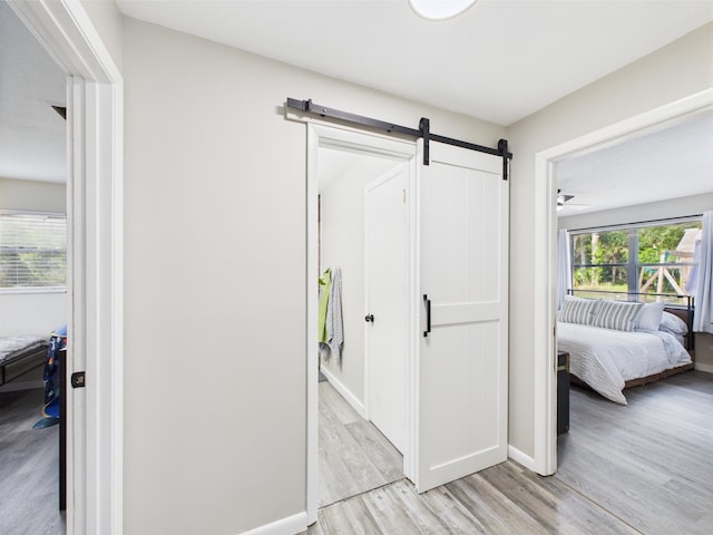 hall featuring a barn door, light wood finished floors, and baseboards
