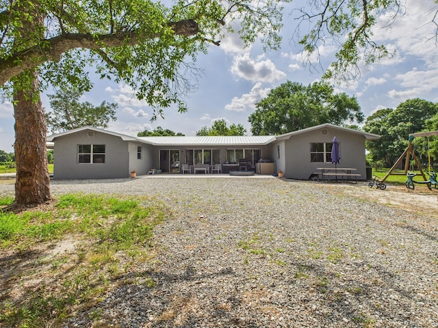 rear view of house featuring stucco siding, metal roof, a playground, and a patio